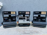 Front and slight angle view of three Polaroid instant cameras, two OneStep CloseUp and one Sun 600 LMS model in the center.