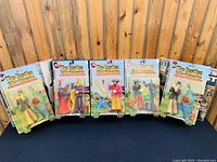 Front view of five unopened Beatles Yellow Submarine Sgt Peppers Lonely Hearts Club Band action figures in sealed original packaging on black cloth against wooden panel wall.