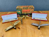 Photo of lot showing two Shanghai pens in cases, two metal firefly door knockers, and Starbucks collectible tin truck on wood surface with gray wall background.