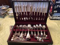 Full set of silverware displayed in original box showing knives, forks, spoons, and serving pieces with intricate floral handles.