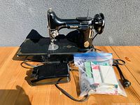Front angled view of Singer Featherweight 221 sewing machine with attached power cord, foot pedal, and plastic bag of accessories