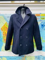 Front view of navy blue Topman men's wool blend peacoat on mannequin against map backdrop.