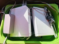 Two white Nintendo Wii consoles placed in a green bin with cables connected, side view.