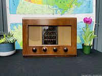 Front view of Bush AC11 valve radio showing wooden casing, cloth speaker grilles, four control knobs, and tuning dial.