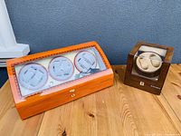 Photo showing large three-watch wood-finished watch winder next to a smaller Konsini two-watch winder, placed on a wood surface.
