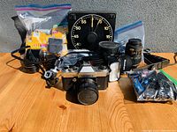 Overview of all items including Yashica camera body with mounted lens, several lenses, external flashes, camera strap, bags of film rolls, and a large mechanical timer.