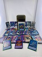 Overview of many Yu-Gi-Oh trading cards including holographic ones spread in front of a metal card tin container.