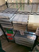 Photo of multiple plastic storage boxes stacked on metal shelves containing labeled craft supplies including beads, embellishments, and papers.