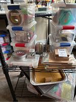 Wider view of the storage rack with multiple containers of art supplies, sponges, cups, and some boxed paper sheets