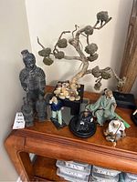 Full view of all Asian male figures and faux tree placed on wooden furniture.