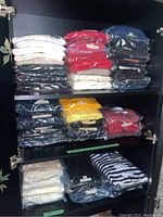 Shelves with neatly folded men's sweaters and cardigans in vacuum sealed plastic packaging and loose stacks, showing a variety of colors including white, red, navy blue, black, yellow, and striped patterns.