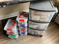 Photo shows clear plastic storage boxes with red, green and blue locking clips and a 3-drawer plastic cabinet filled with supplies.