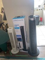 Three tower fans shown. One white Sunbeam fan, one black and silver Bionaire fan with digital control panel, and one Bionaire fan in its original box.