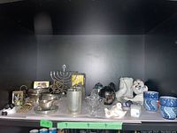 Wide view of all decorative items including tea cups, metal pitchers, candle holder, bird figurines, tray, vases, and oriental box