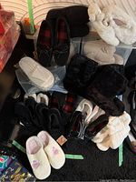 Photo showing assortment of slippers, moccasins, booties, mostly in black and white colors, various styles for indoor wear.