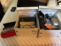 Overall view of boxes labeled 'Glasses' and 'Hearing Aids' showing multiple eyeglass cases, eyeglasses, and hearing aid supplies.