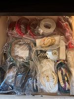 Top view of various ladies fashion belts packed in a drawer, showing red, white, black belts and some rope style belts with gold buckles