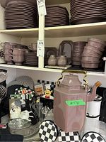 Photo of shelves with stacked Mikasa plates, bowls, cups, and creamer and sugar set. Large geometric pink/purple ceramic teapot in front.