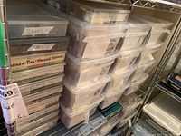 Shelving with multiple stacked plastic containers labeled with sewing and crafting supplies including brads and machine needles.