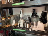 Shelf containing Betty Crocker food processor, hand mixer, coffee grinder, and other kitchen appliances.