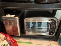 View of Black and Decker toaster oven and stainless steel cooler unit side by side on a shelf