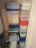 Stacked plastic storage containers in clear plastic with blue, red, and teal lids. Various sizes with some containers labeled.