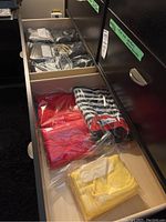 Drawer showing multiple individually plastic-packed T-shirts in yellow, red, black and white stripes with red collar, and other colors.