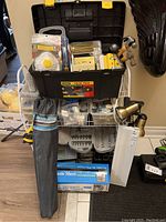 Photo showing full rack with toolbox on top and various tools and hardware including a tripod stand, plastic sheeting boxes and a white tool fixture.