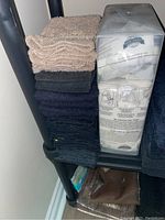 Stacked brown, black, and dark blue towels with clear-packaged shower curtain hooks on a shelf.