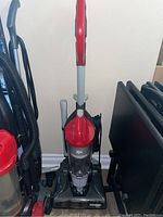 Full view of the Dirt Devil upright vacuum showing red handle, black base, and attached hose.