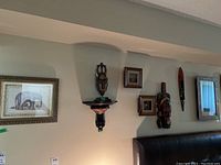 Overall view of the wall with multiple hanging items including the carved masks, framed elephant print, 3D animal art and mirror.