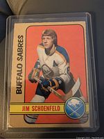 Front side of 1972-73 O.P.C. Jim Schoenfeld rookie hockey card showing player image and team logo.