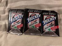 Three sealed 1990-91 Upper Deck High Series NHL Hockey wax packs on a beige fabric surface.