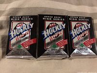 Three sealed wax packs of 1990-91 Upper Deck NHL Hockey High Series hockey cards shown side by side on a fabric surface.