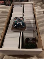 Long cardboard box with multiple separated stacks of trading cards, mostly white backs, some visible front cards featuring football players in various poses and styles.