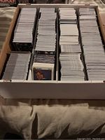 Overview of the box containing tightly packed rows of assorted trading cards, mainly showing backs of cards with some fronts visible at the ends.