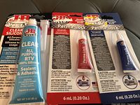 Photo showing three JB Weld adhesive products: one clear silicone sealant and two Perma-Lock adhesive tubes in red and blue packaging.