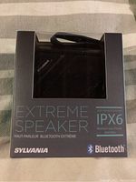 Front view of boxed Sylvania Extreme Speaker showing product inside and packaging with IPX6 and Bluetooth markings.