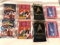 Photo showing eight packs of non-sport wax packs laid out on a flat surface: 2 Flintstones Modern Stone Age Family packs, 2 Hercules The Animated Series packs, 2 Star Trek packs, and 2 TLC sticker packs.