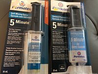Photo of two Permatex 5 Minute Epoxy products in original packaging: one 14 ml self-mixing cartridge and one 25 ml general purpose gel tube.