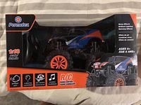 Front view of the unopened 1/18 scale Permatex radio controlled monster truck in packaging showing truck with blue, black, orange colors and features.