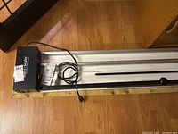 Full length view of the sealing machine showing the silver band and black control box with power cord on wooden floor.