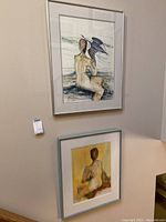 Two framed paintings on a beige wall showing nude figures, one with a bird and one seated with back view.