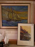 Overview of both framed paintings displayed against a brick wall