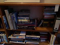 Bookshelves filled with mixed hard and soft cover books with various titles including some art books and novels.