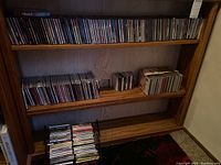 Full shelf view showing multiple rows of CDs in jewel cases and box sets in a wooden shelf.