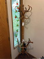Wooden coat rack in corner near stained glass window, with some umbrellas and canes stored in bottom ring holder