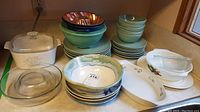 Overall view of stacked bowls, plates, vintage casserole dish, and clear glass bakeware on kitchen counter.
