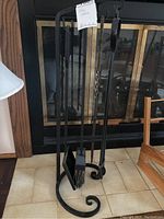 Full view of the iron fireplace tool stand with four hanging tools in front of a fireplace