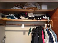 Closet section with shelves holding folded scarves, hats, and umbrellas above hanging rack with coats and jackets